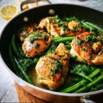 Four golden brown chicken breasts resting on bright green beans in a skillet, topped with fresh parsley.