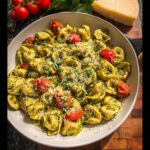 A close-up overhead view of One-Pot Pesto Tortellini with Cherry Tomatoes garnished with Parmesan and basil.