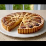 A beautiful Pear Almond Frangipane Tart with one slice removed, topped with sliced pears and almonds.