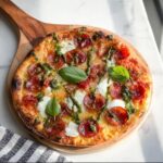 A freshly baked Pepperoni Burrata Pizza with Basil Pesto drizzled over melted cheese and topped with fresh basil leaves.