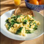 Fluffy scrambled eggs mixed with wilted spinach served with whole wheat toast, part of a Protein-Packed Breakfast-for-Lunch Scramble.