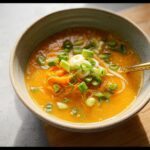 Close-up of a vibrant orange Quick Carrot & Onion Miso Bowl topped with fresh scallions and noodles.