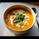 Close-up of a creamy, orange Red Lentil Coconut Curry Soup topped with coconut cream swirl and fresh cilantro.