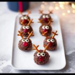Six festive Reindeer Pretzel Bites decorated with candy eyes and red noses, arranged on a white platter.