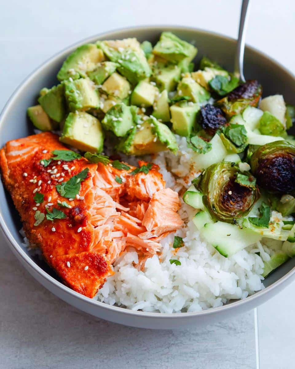 Close-up of a Salmon Avocado Protein Bowl featuring flaky salmon, diced avocado, white rice, and roasted Brussels sprouts.