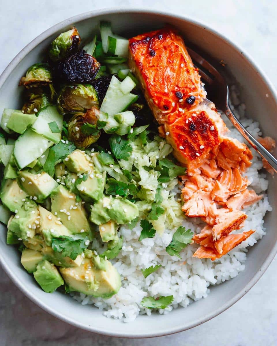 Overhead view of a Salmon Avocado Protein Bowl featuring flaky salmon, diced avocado, rice, and roasted Brussels sprouts.