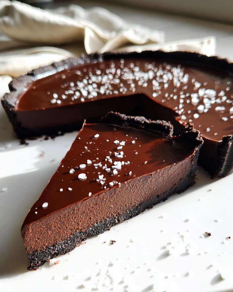A slice of rich Chocolate Ganache Tart with a dark crust, topped with flaky sea salt.