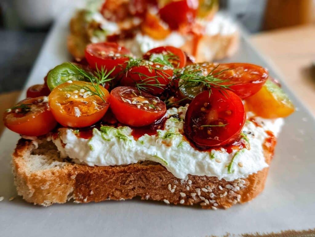 Close-up of Savory Cottage Cheese Toast topped with halved cherry tomatoes, dill, and sesame seeds.