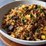 A close-up of a bowl filled with Simple Beef & Veggie Fried Rice topped with green onions and sauce.