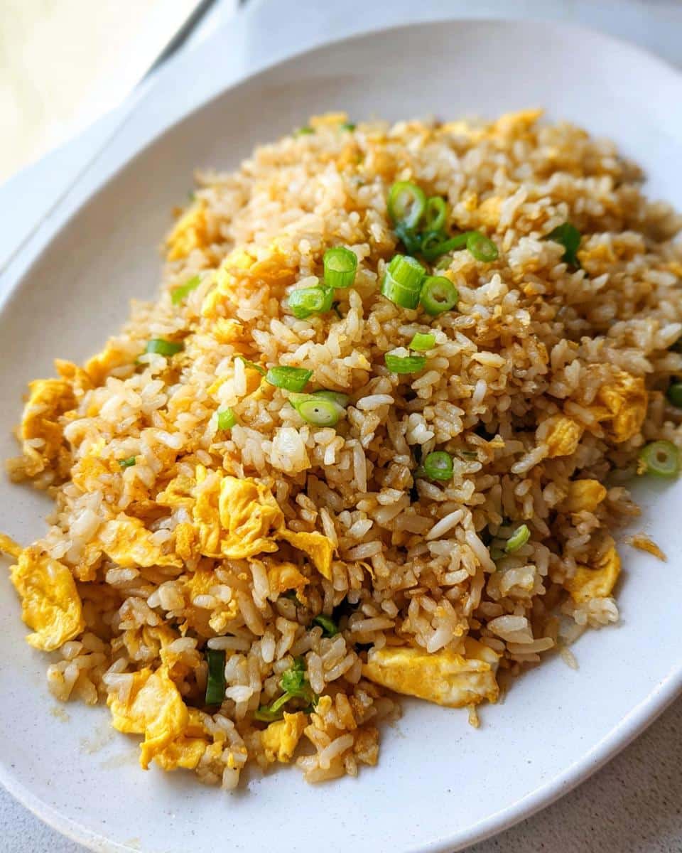A close-up of Simple Egg Fried Rice, featuring fluffy rice, scrambled egg pieces, and chopped green onions on a white plate.