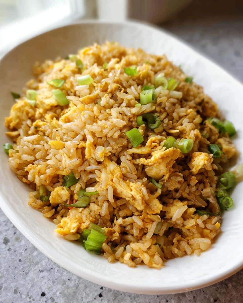 Close-up of a white oval plate piled high with Simple Egg Fried Rice garnished with bright green chopped scallions.