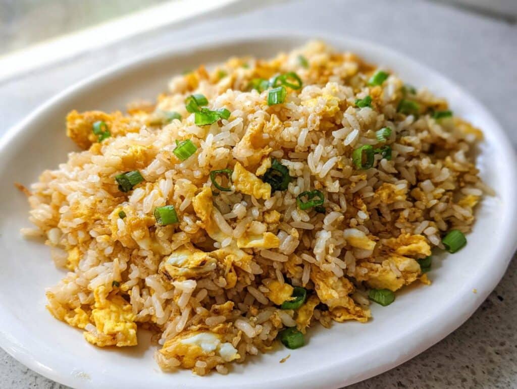 A close-up serving of Simple Egg Fried Rice, featuring fluffy rice, scrambled egg pieces, and green onion garnish.