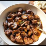 Close-up of juicy Skillet Steak Bites in Mushroom Gravy, garnished with fresh thyme, served in a white bowl.