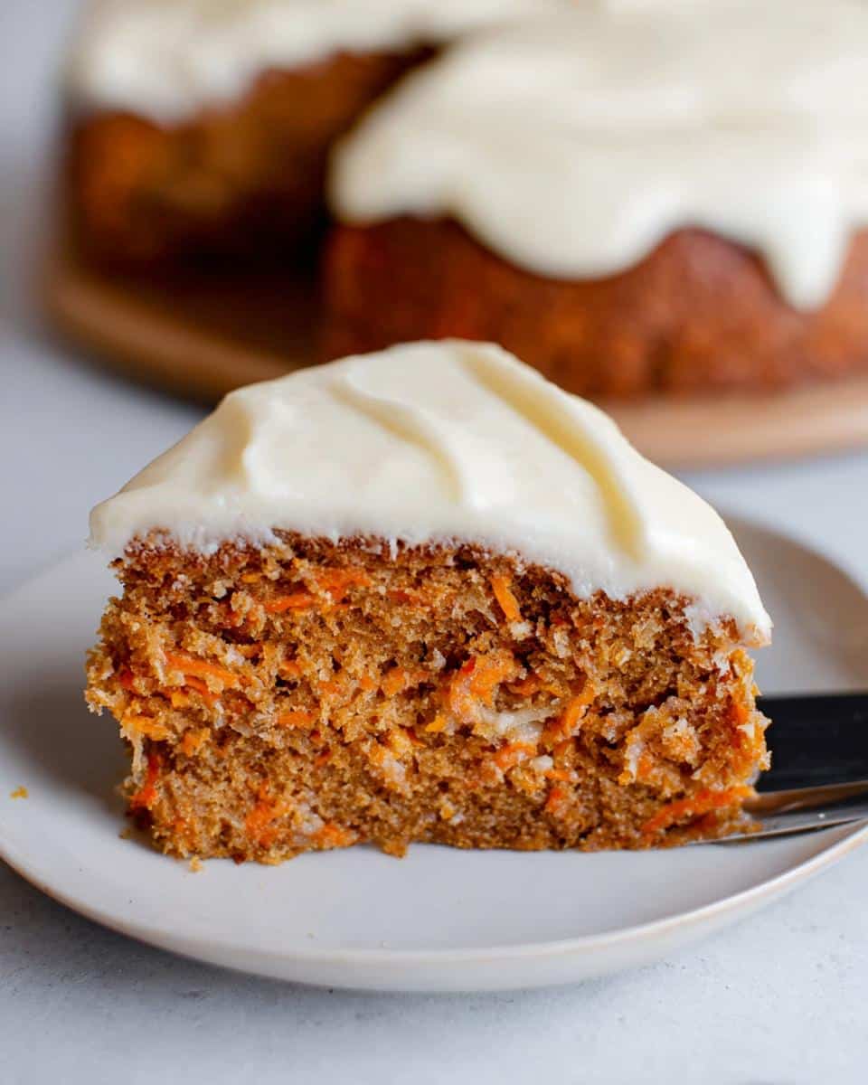 Close-up of a moist slice of Thermomix Carrot Cake with thick cream cheese frosting on a white plate.