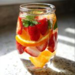 Close-up of Slimming Strawberry Detox Water infused with orange slices and mint leaves in a clear glass jar.