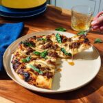 A slice being lifted from a Spicy Sausage & Honey Pizza, showing drizzled honey.