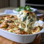 A spoonful of cheesy Spinach Alfredo Tortellini Bake showing a dramatic cheese pull over the baking dish.