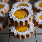 Two stacked Jam-Filled Linzer-Style Cookies dusted heavily with powdered sugar, showing bright yellow passion fruit filling.