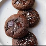 Close-up of four dark, fudgy Tahini Chocolate Chunk Cookies topped with flaky sea salt.
