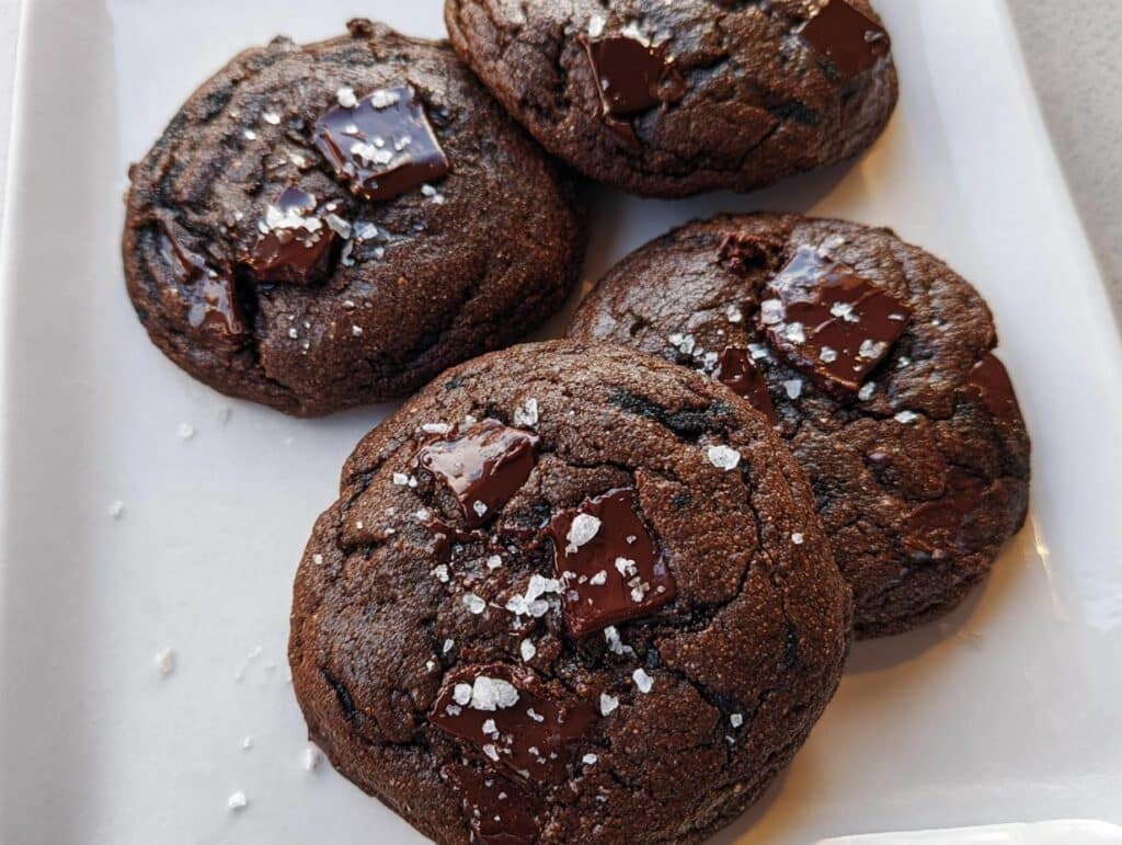 Four dark chocolate Tahini Chocolate Chunk Cookies topped with melted chocolate chunks and flaky sea salt.