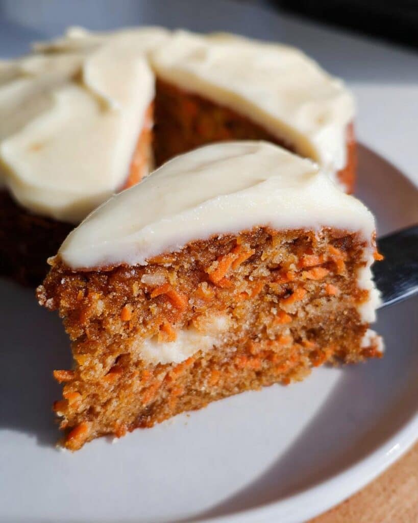 Close-up of a slice of moist Thermomix Carrot Cake with visible shredded carrots and thick cream cheese frosting.