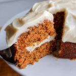 A close-up of a slice being lifted from a rich Thermomix Carrot Cake with Cream Cheese Frosting.