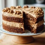 A two-layer Thermomix Coffee Walnut Cake with coffee buttercream frosting, topped with walnuts, one slice removed.