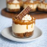 Close-up of an individual Thermomix Salted Caramel Cheesecake served in a glass with caramel drizzle and a chocolate bar piece.