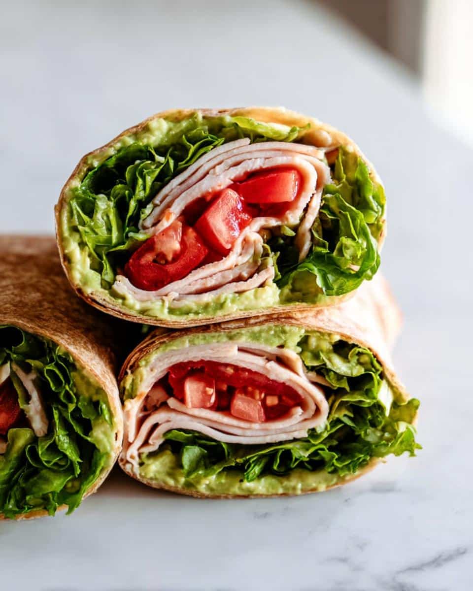 Close-up of a Turkey & Avocado Whole Wheat Wrap cut in half, showing layers of turkey, tomato, lettuce, and avocado spread.