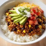 Close-up of a Turkey Taco Rice Bowl featuring seasoned ground turkey, black beans, corn, white rice, avocado, sour cream, and diced tomatoes.
