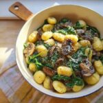 A bowl of Vegetarian Gnocchi with Spinach and Mushroom-Butter Sauce topped with grated cheese.