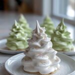 A beautifully piped white Tree Meringue Cookie decorated with pastel sprinkles, sitting on a white plate.