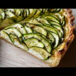 A close-up slice of Zucchini & Goat Cheese Tart showing overlapping zucchini rounds over a creamy filling and golden crust.