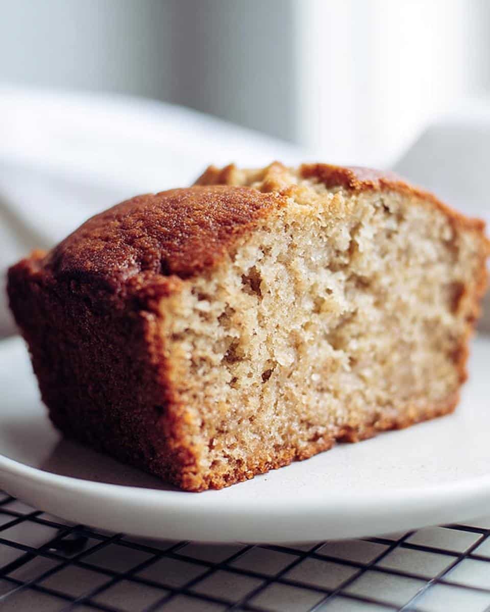 A close-up of a moist slice of 2-Banana Easy Banana Bread resting on a white plate.