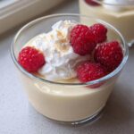 Close-up of a glass serving of 5-Ingredient Vanilla Pudding Dessert topped with whipped cream, fresh raspberries, and brown sugar.
