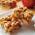Close-up of two rich Apple Cinnamon Crumble Bars stacked slightly on a white plate, featuring an oat topping.