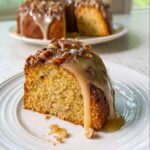 A close-up of a slice of Baileys Irish Cream Cake topped with a thick caramel glaze and chopped pecans.