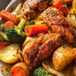 Close-up of perfectly seasoned, browned chicken pieces nestled among roasted potatoes, bright orange carrots, and green broccoli in a Baked Chicken & Veggie Tray Bake.