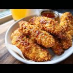 Close-up of crispy, golden Baked Honey Mustard Chicken Tenders drizzled with glaze, served with dipping sauce.