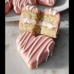 Close-up of a heart-shaped Bakery Style Valentine Cake, cut in half to show layers of sponge and cream filling.