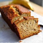 Close-up of a freshly baked loaf of Banana Bread With Olive Oil, partially sliced, showing a moist crumb.