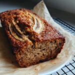 Close-up of a freshly baked loaf of Banana Walnut Bread with a caramelized crust and sliced banana topping.