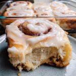 A close-up shot of one soft, gooey homemade cinnamon roll with thick white icing, showing a bite taken out.