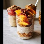 Close-up of a jar containing the Best Overnight Oats Recipe, layered with oats, chia pudding, and topped with fresh peach slices and granola.