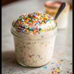 Close-up of Birthday Cake Overnight Oats in a mason jar, topped with frosting and colorful sprinkles.