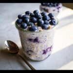 Close-up of Blueberry Almond Overnight Oats in a glass jar, topped generously with fresh blueberries.