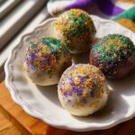Four Boozy King Cake Truffles, three white chocolate and one dark chocolate, covered in purple, green, and gold sprinkles.