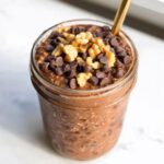 Close-up of Brownie Batter Overnight Oats in a jar, topped with chocolate chips and walnuts.