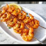 Close-up of grilled Cajun Shrimp Skewers seasoned with spices, garnished with parsley and a lemon wedge.