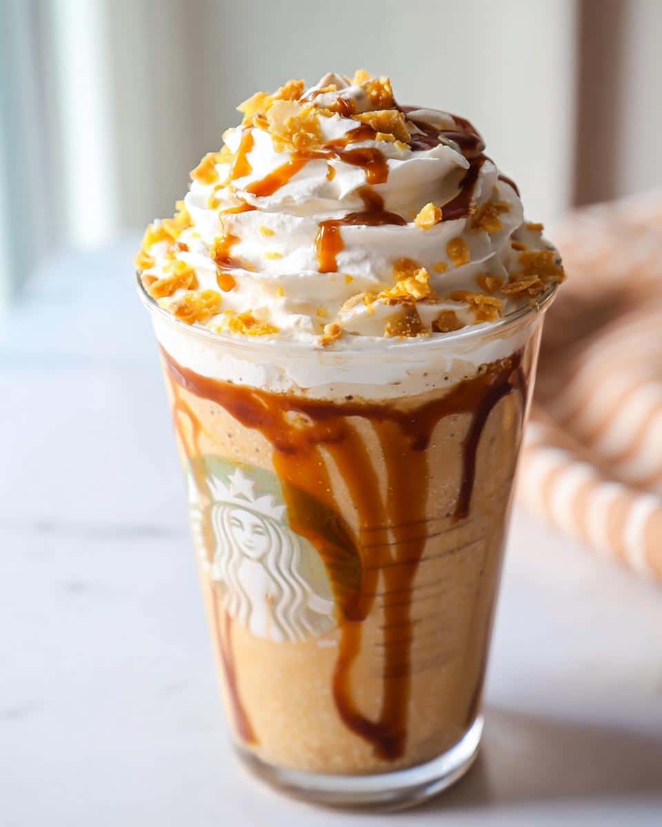 A close-up of a Caramel Ribbon Crunch Frap Copycat topped high with whipped cream, caramel drizzle, and crunchy topping.